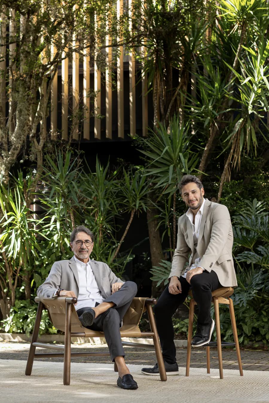 Dois arquitetos sentados em banquetas diante de um jardim de folhagens densas